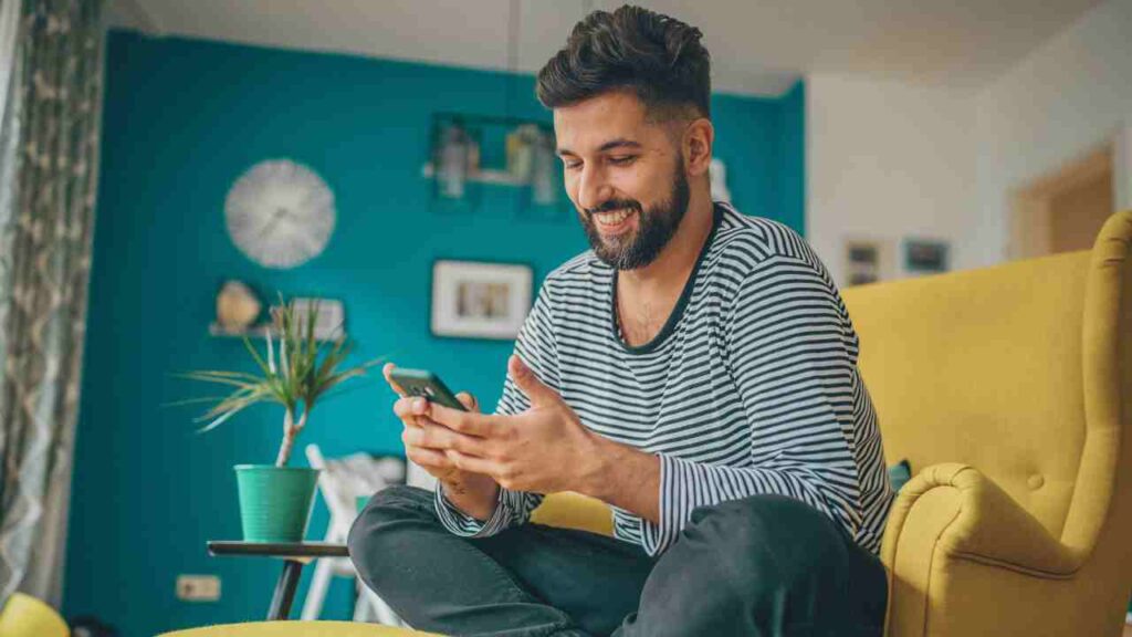 A man seated on a yellow chair, holding a phone in his hand.